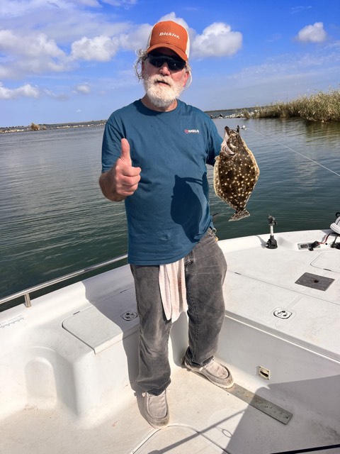 Man on boat holding a fish, giving a thumbs-up gesture, blue water and sky background.
