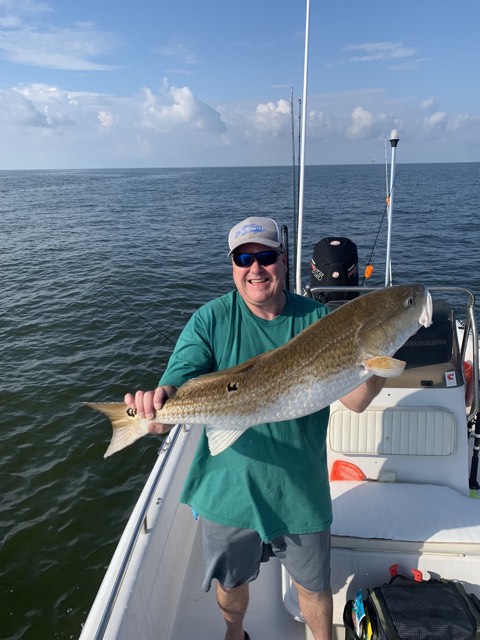 Man holding a large redfish on a boat in open water. Cloudy sky.